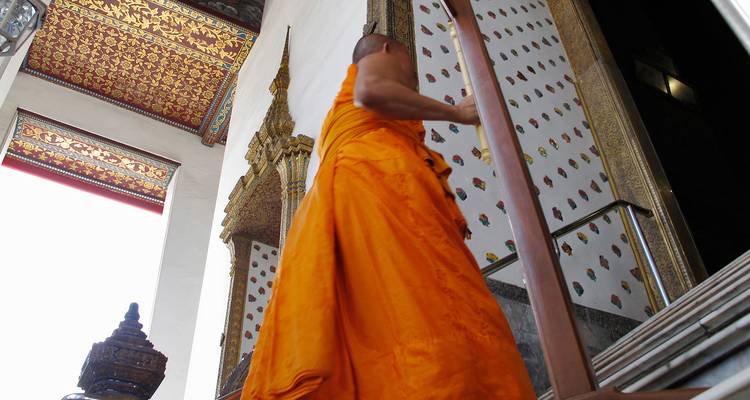 Monje con túnica naranja vibrante sube las escaleras del templo decoradas con patrones intrincados.