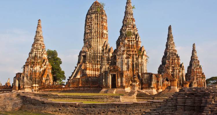 Plano general de las ruinas del templo de Ayutthaya con múltiples prangs imponentes bajo la cálida luz del atardecer.