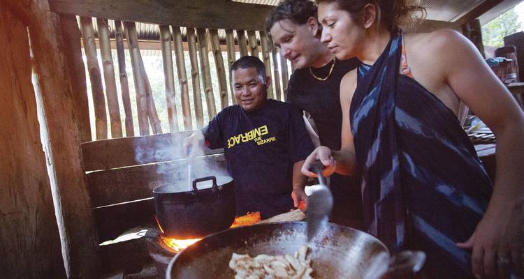 Los viajeros se unen a un guía local para cocinar sobre un fuego abierto dentro de una cocina de madera rústica.