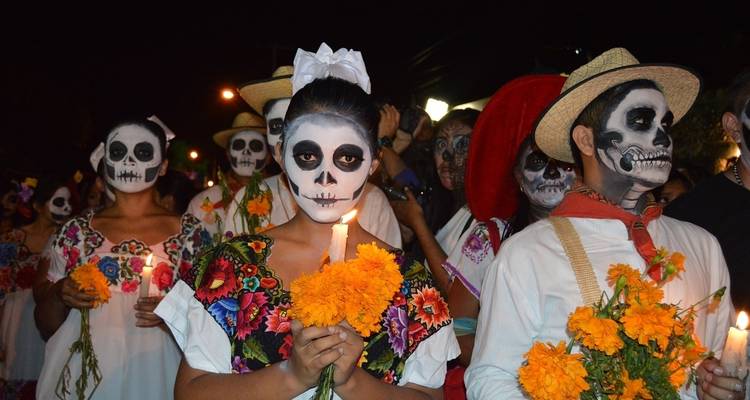 Des personnes en costumes traditionnels du Jour des Morts tenant des bougies et des fleurs.
