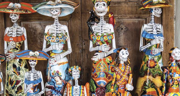 Figurines de squelettes en céramique colorées du Jour des Morts exposées contre une porte en bois