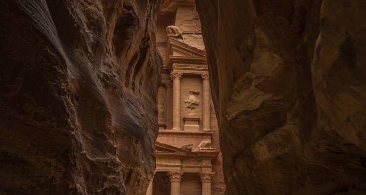 View of Petra Treasury framed between narrow sandstone canyon walls.
