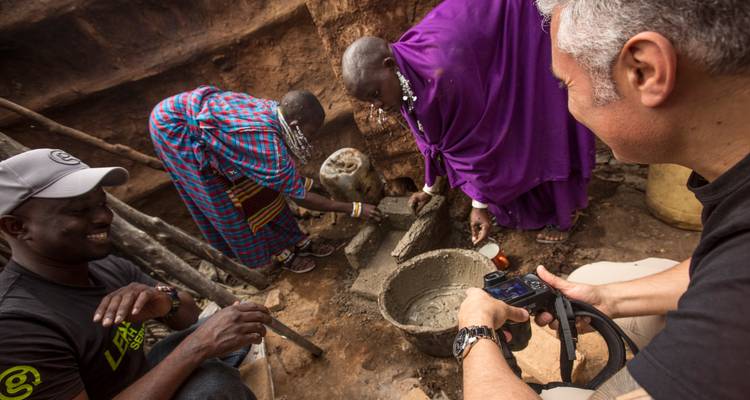 Viajeros y aldeanos Maasai colaboran en un proyecto artesanal de arcilla y cemento dentro de un recinto de tierra.