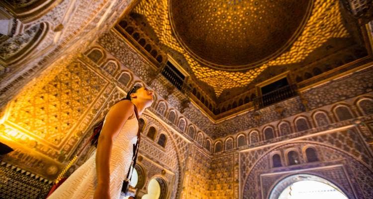 Vrouw die omhoog kijkt naar het sierlijke gouden mozaïekplafond in de luxe hal van het Alcázar.