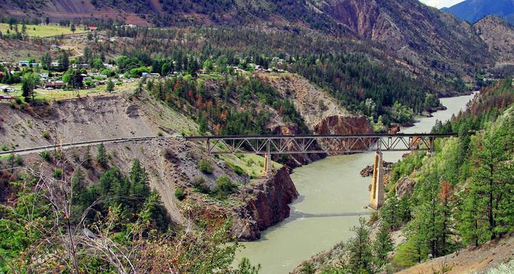 Un puente ferroviario atraviesa un profundo cañón de río rodeado de colinas verdes y escarpadas con un pequeño asentamiento.