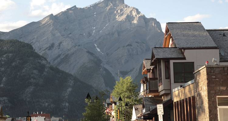 Tiendas encantadoras en la avenida Banff con imponentes montañas de fondo bajo la suave luz del atardecer.
