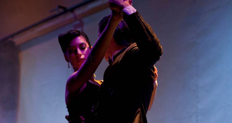 Des danseurs de tango élégants se produisent sous un éclairage de scène dramatique à Buenos Aires.