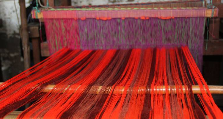 Primer plano de hilos de colores brillantes siendo tejidos en un telar tradicional