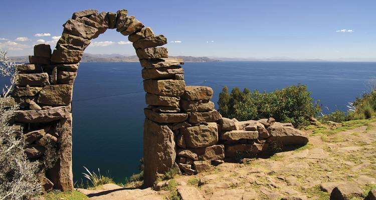 Puerta de arco de piedra con vistas a las aguas azul profundo de un enorme lago de alta montaña