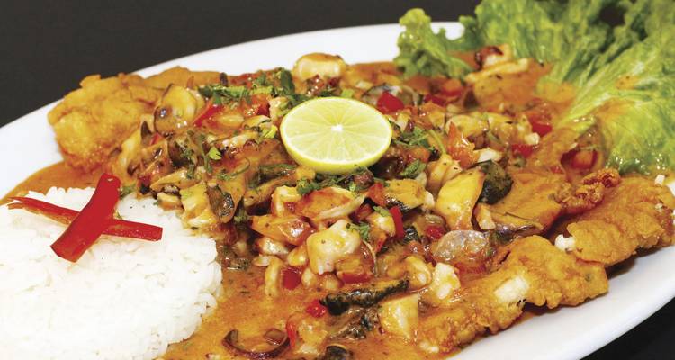 Plate of Peruvian fish stew with rice, lime slice and lettuce garnish