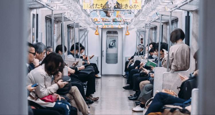 Forensen zitten rustig in een Japanse metrotrein, veel van hen gefocust op hun telefoons.