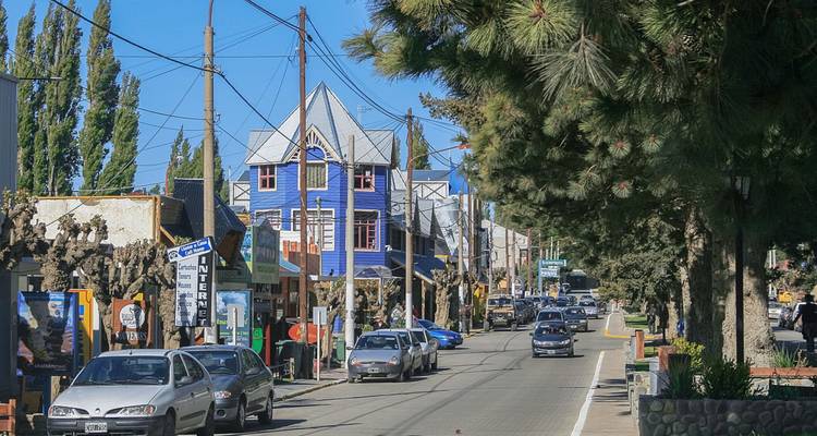 Kleine patagonische Stadt mit einer Hauptstraße, die von bunten Holzgebäuden, Autos und hohen Kiefern unter klarem Himmel gesäumt ist