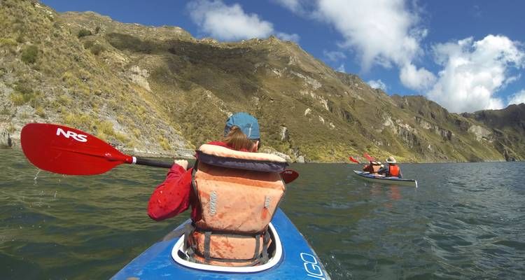 Menschen paddeln mit dem Kajak auf einem von Bergen umgebenen See.