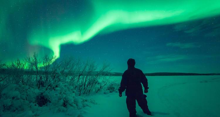 Reisender als Silhouette vor lebhaftem grünem Nordlicht, das über verschneite Landschaft wirbelt