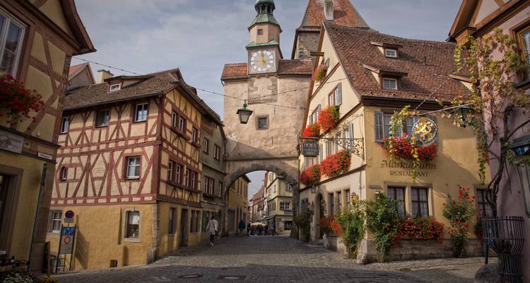 Tour de porte médiévale et maisons à colombages ornées de géraniums rouges le long d'une rue tranquille de Rothenburg.