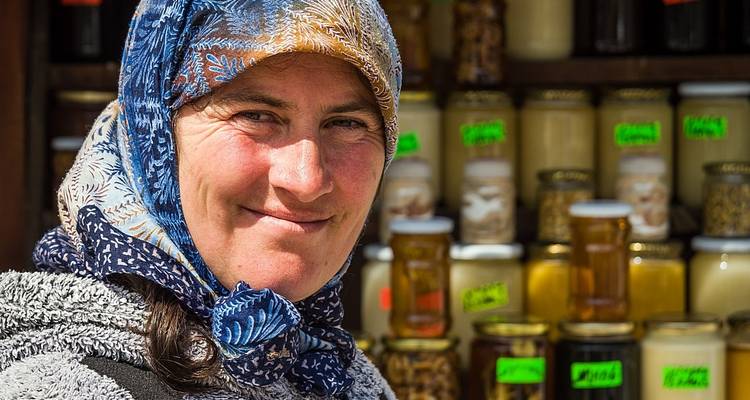 Portrait d'une femme avec un foulard et des pots de miel en arrière-plan.