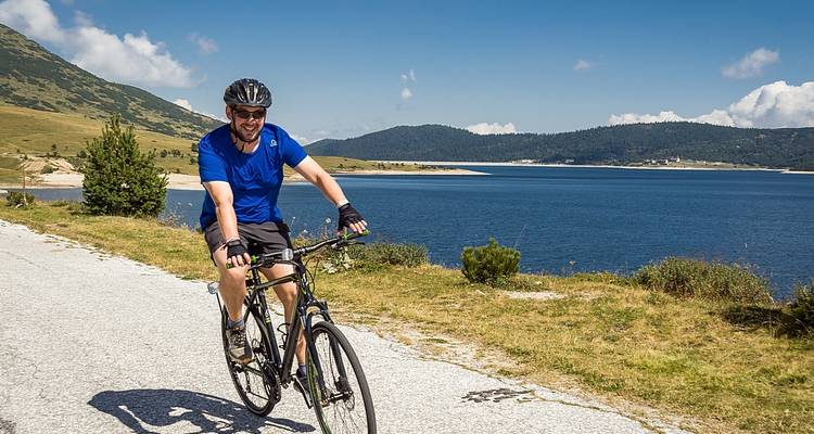 Cycliste roulant le long d'un lac avec des montagnes en arrière-plan.