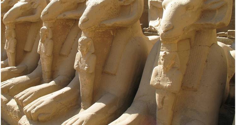 Une rangée de statues représentant des figures à tête de bélier dans un cadre antique.