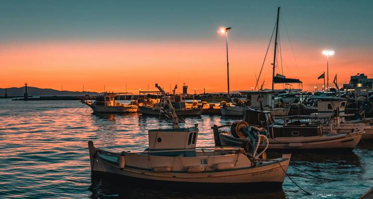 Traditionele vissersboten schommelen in een haven onder een levendig oranje zonsonderganghemel op een Grieks eiland.