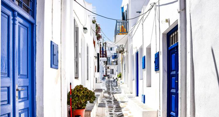 Heldere, smalle steeg met witte Cyclische huizen en blauwe deuren met een patroonvormig stenen pad in Mykonos.
