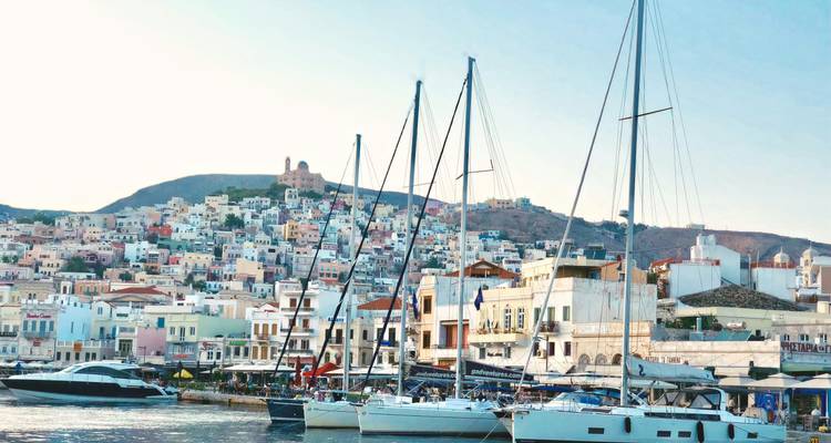 Marina vol zeilboten met op de achtergrond een kleurrijk bergstadje op een heldere dag in Syros.