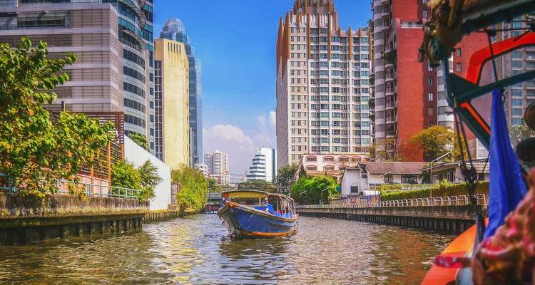 Ein Longtail-Boot navigiert durch einen Kanal, der von modernen Hochhäusern in dem geschäftigen Bangkok gesäumt wird.