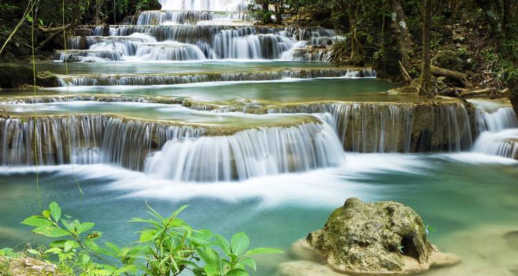 Gestufte türkisfarbene Becken des Erawan-Wasserfalls, die durch den üppigen Dschungel in Thailand hinabstürzen.