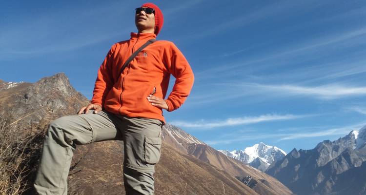 Persona con una chaqueta naranja posando con confianza con montañas de fondo