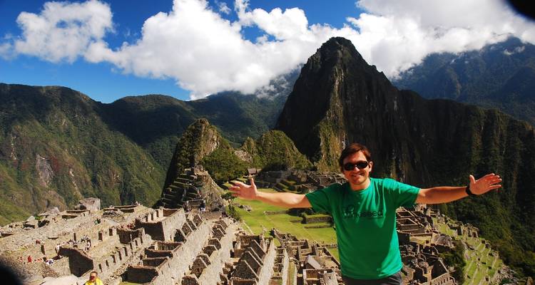 Turista posando con los brazos extendidos ante las ruinas de Machu Picchu.