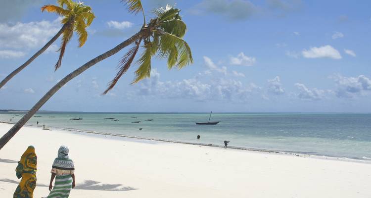 Zandstrand in Zanzibar met mensen die wandelen onder palmbomen