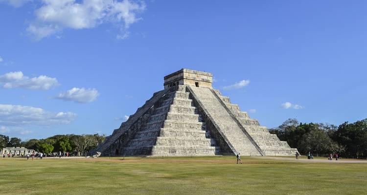 Iconic El Castillo pyramid rising above a grassy plaza at Chichen Itza on a clear day.