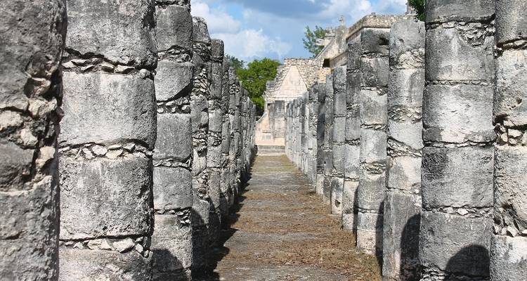 Row of weathered stone columns forming a narrow corridor at an ancient ruins site.