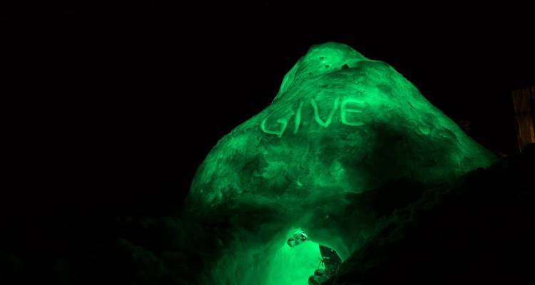 Leuchtend grüne Eisskulptur in einer dunklen Umgebung mit eingemeißeltem 'GIVE'.