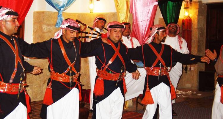 Mannen in traditionele klederdracht die dansen, met kleurrijke doeken op de achtergrond.