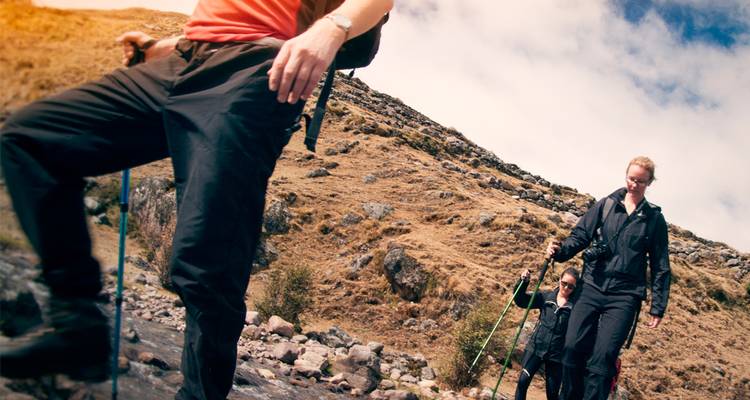 Los excursionistas con bastones de trekking cruzan un arroyo de montaña rocoso en un día soleado.