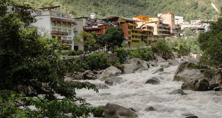 Río veloz fluyendo entre la vegetación de la selva y el colorido pueblo de Aguas Calientes.