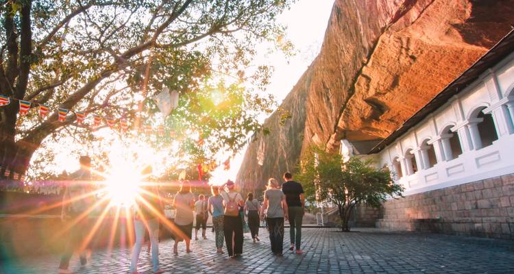 A group of people walking towards a rock temple with sun flares and flags.