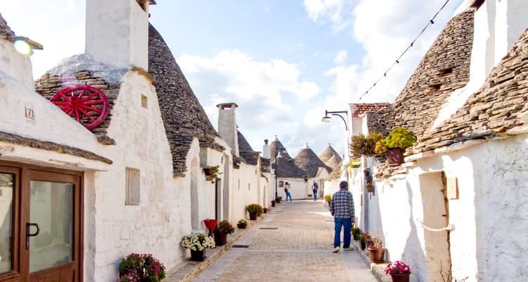 Pintoresca callejuela estrecha bordeada de casas trulli encaladas con tejadillos de piedra puntiaguda, unos pocos visitantes paseando por aquí.