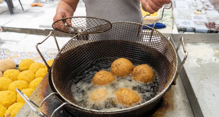 Straatverkoper bakt gouden arancini-balletjes in hete olie op een buitenmarkt.