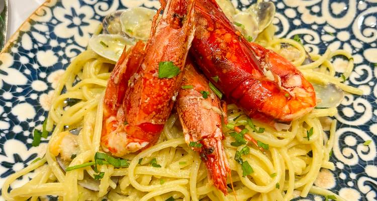Gros plan de linguine aux crevettes garnies de persil sur une assiette en céramique à motifs.