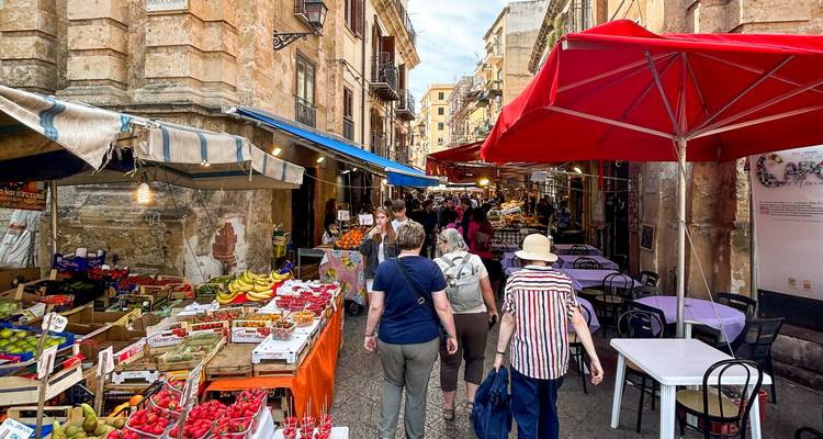 Les acheteurs se promènent dans une rue animée de marché de produits frais bordée d'étals colorés à Palerme.