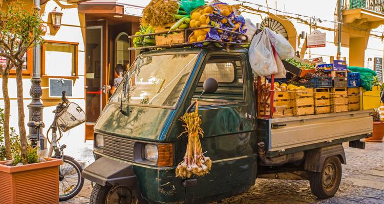 Un camion Ape trois roues coloré chargé de produits frais dans une charmante ruelle sicilienne.