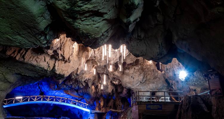 Las estalactitas iluminadas cuelgan del techo de una caverna de piedra caliza alta con iluminación azul de acentuación.