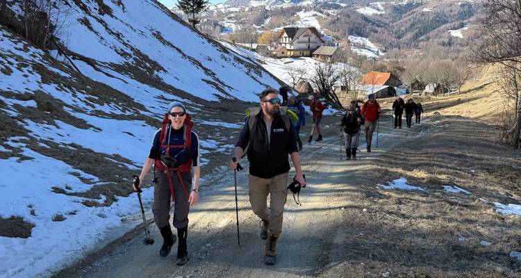 Grupo de caminantes pasan por un valle de pueblo rural de los Cárpatos con parches de nieve de primavera.