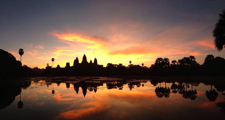 Die schattenhaften Spitzen von Angkor Wat spiegeln sich in stillem Wasser vor einem glühend roten Sonnenaufgangshimmel.