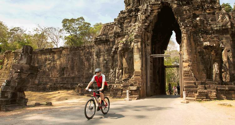 Ein Radfahrer fährt an einem sonnigen Tag durch das imposante Steintor von Angkor Thom.