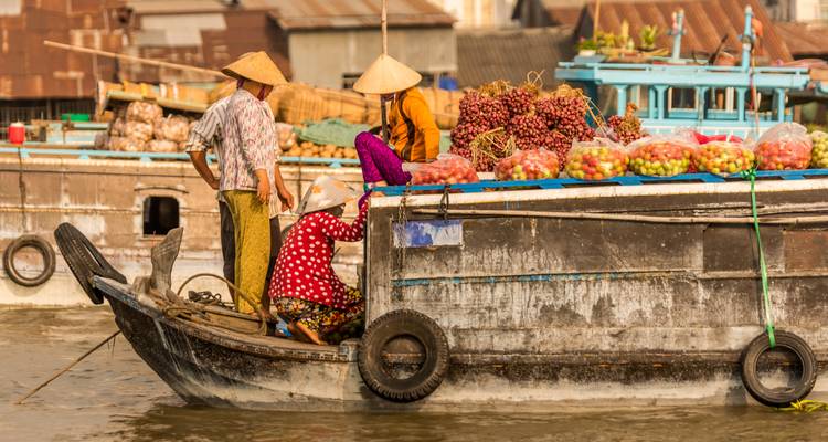Verkäufer auf einem Holzboot verkaufen Fruchtberge auf einem belebten schwimmenden Markt am Mekong.