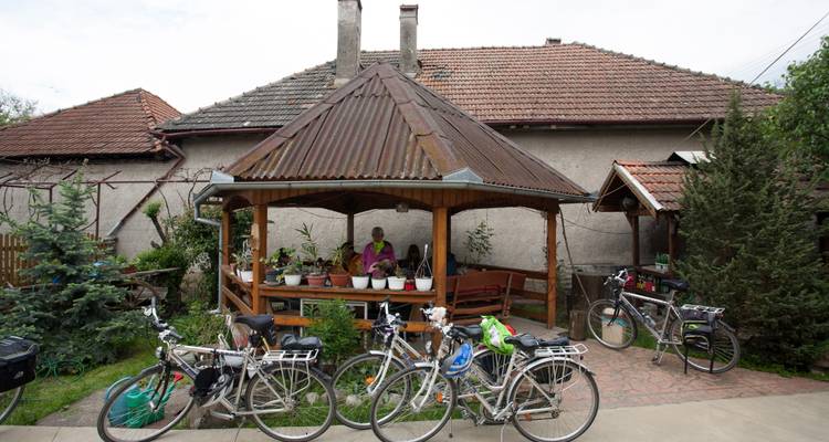 Raststelle für Radfahrer an einem rustikalen Haus mit blumengeschmücktem Holzpavillon und mehreren Tourenrädern, die draußen geparkt sind.