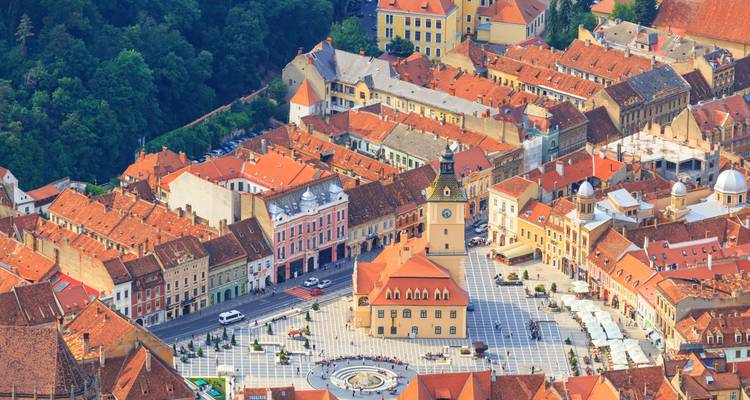 Luftaufnahme von Brasovs farbenfroher Altstadt mit ihrem zentralen Platz und roten Ziegeldächern, eingebettet in eine Hügellandschaft.