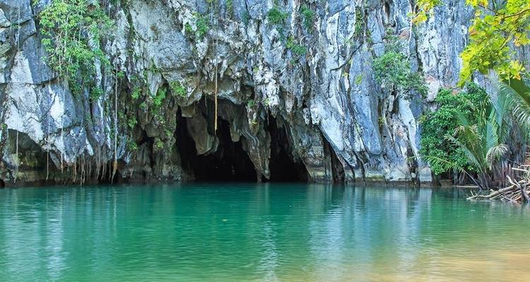 Bouche rocheuse d'une rivière souterraine s'ouvrant sur des eaux émeraude calmes au milieu d'une végétation luxuriante.